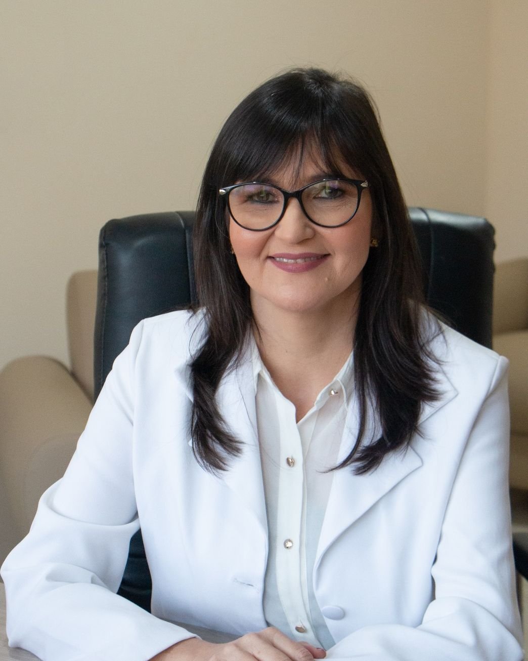 Maria Socorro de Menezes, psicóloga, de blazer branco, sentada à mesa do consultório